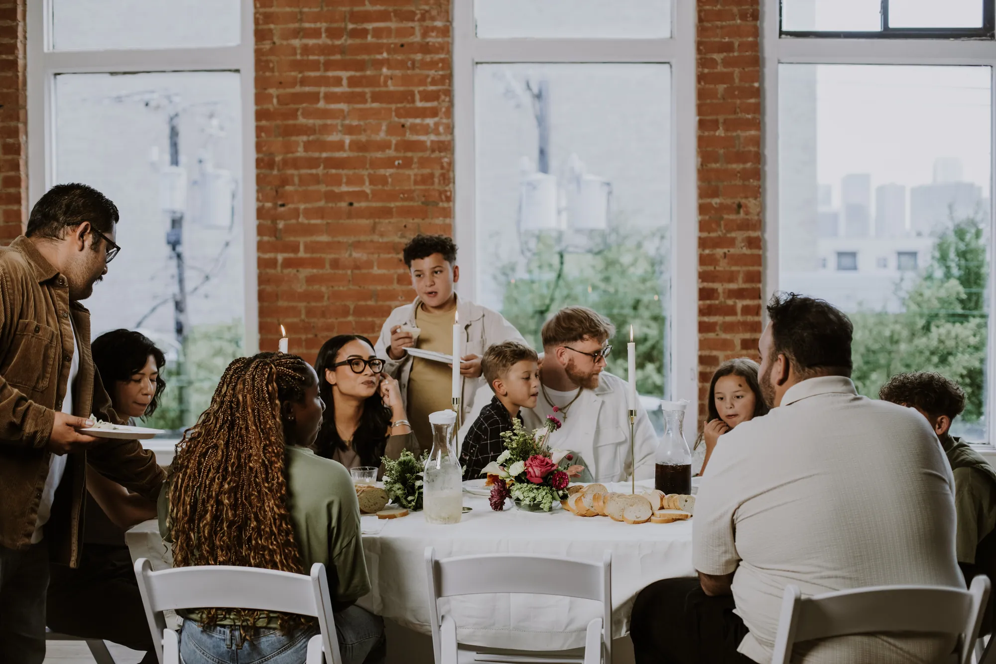 A long table of neighbors eating together in a brick-walled room