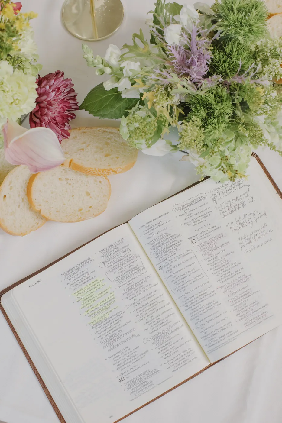 An open Bible beside flowers and bread on the table