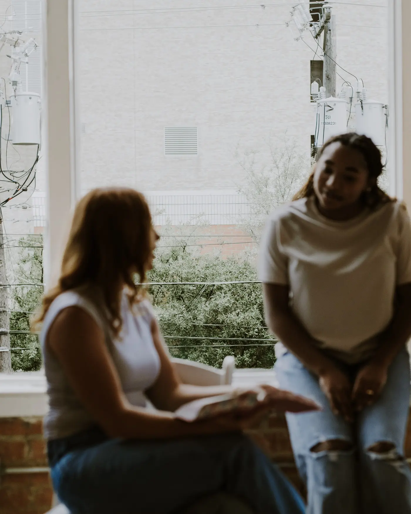 Two women talking on a couch by the window