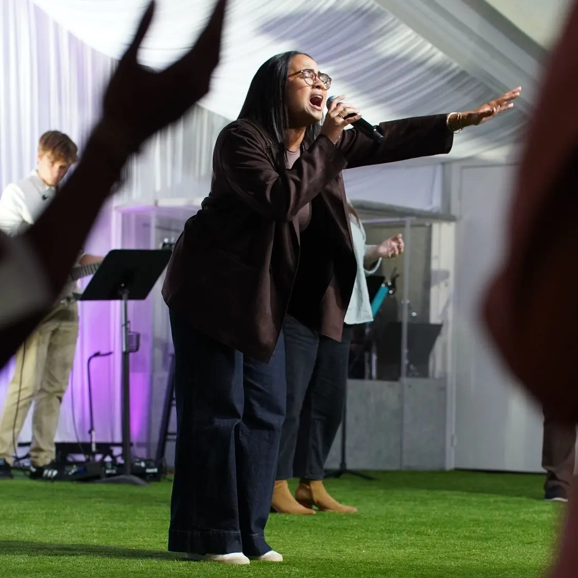 A worship leader singing with her arm outstretched at a Garden Co. Sunday gathering